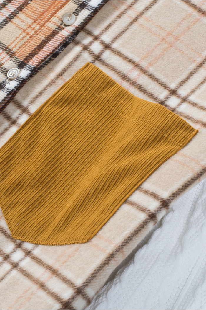 A close-up view of a garment featuring a beige and brown plaid pattern, with a mustard yellow, ribbed patch pocket visible on the left side. The ribbed texture of the pocket contrasts with the woven plaid fabric. 