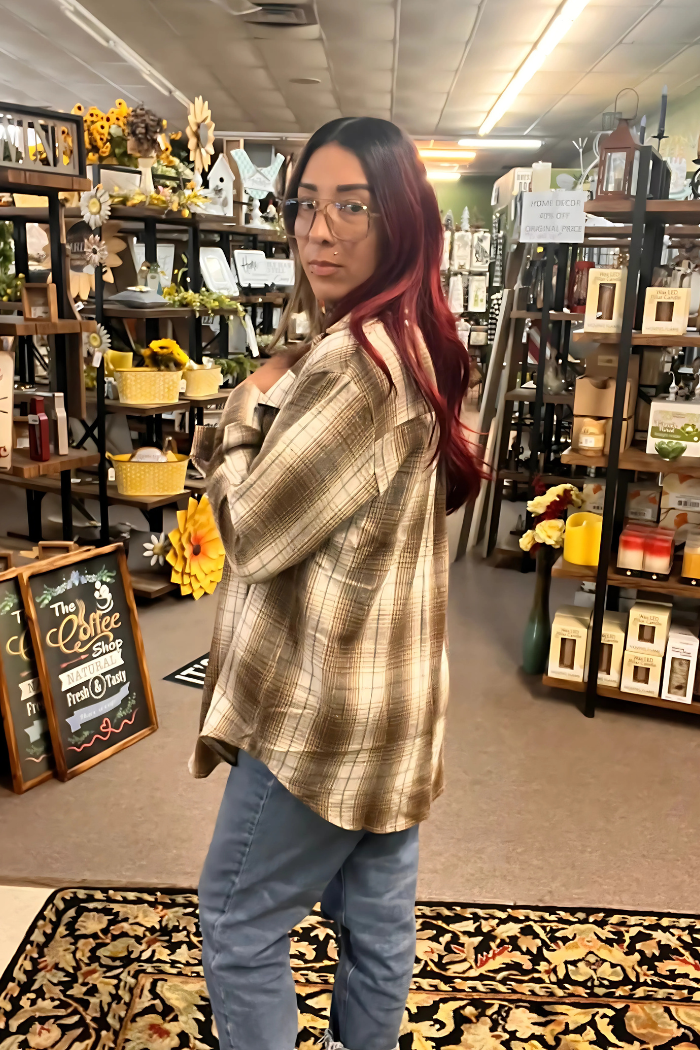 The image shows a young woman with long, dark hair with red highlights, wearing glasses, a brown and tan plaid button-up shirt, and light-wash jeans.
