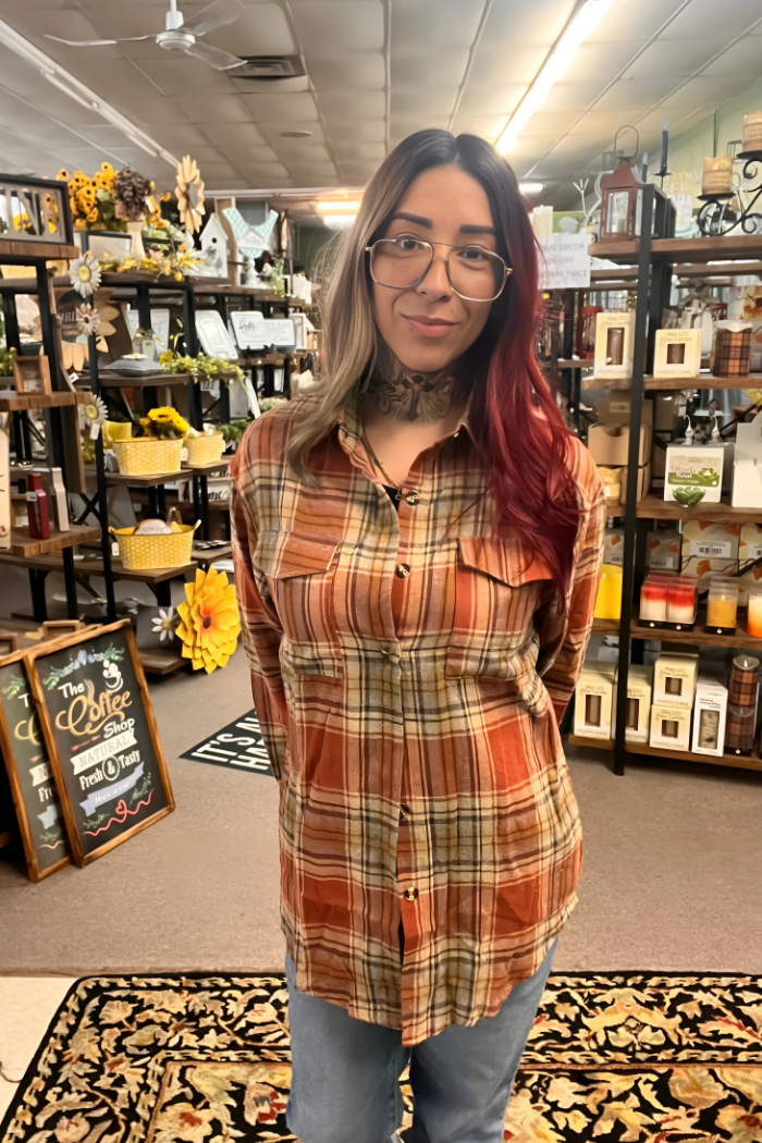 A young woman is wearing a rust-colored plaid flannel shirt with two chest pockets and light-wash blue jeans