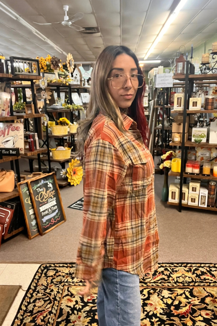 A young woman standing from the side wearing a rust-colored oversized plaid flannel shirt and light-wash blue jeans.