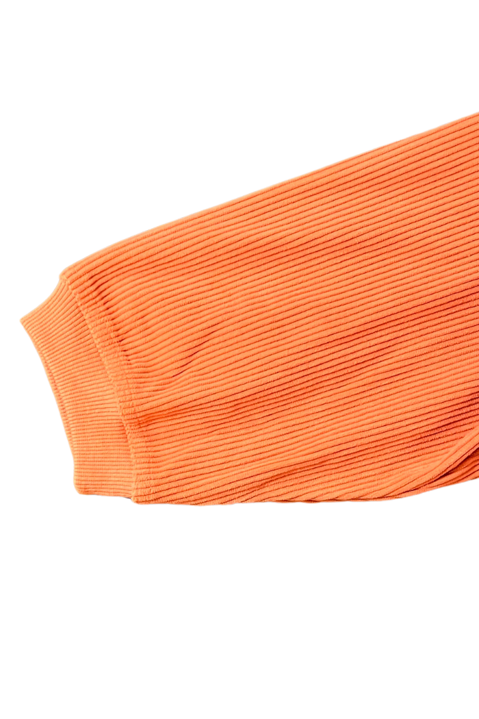 The image shows the sleeve of an orange, ribbed corduroy garment, sweatshirt featuring a ribbed cuff. The fabric has a distinct vertical texture characteristic of corduroy.