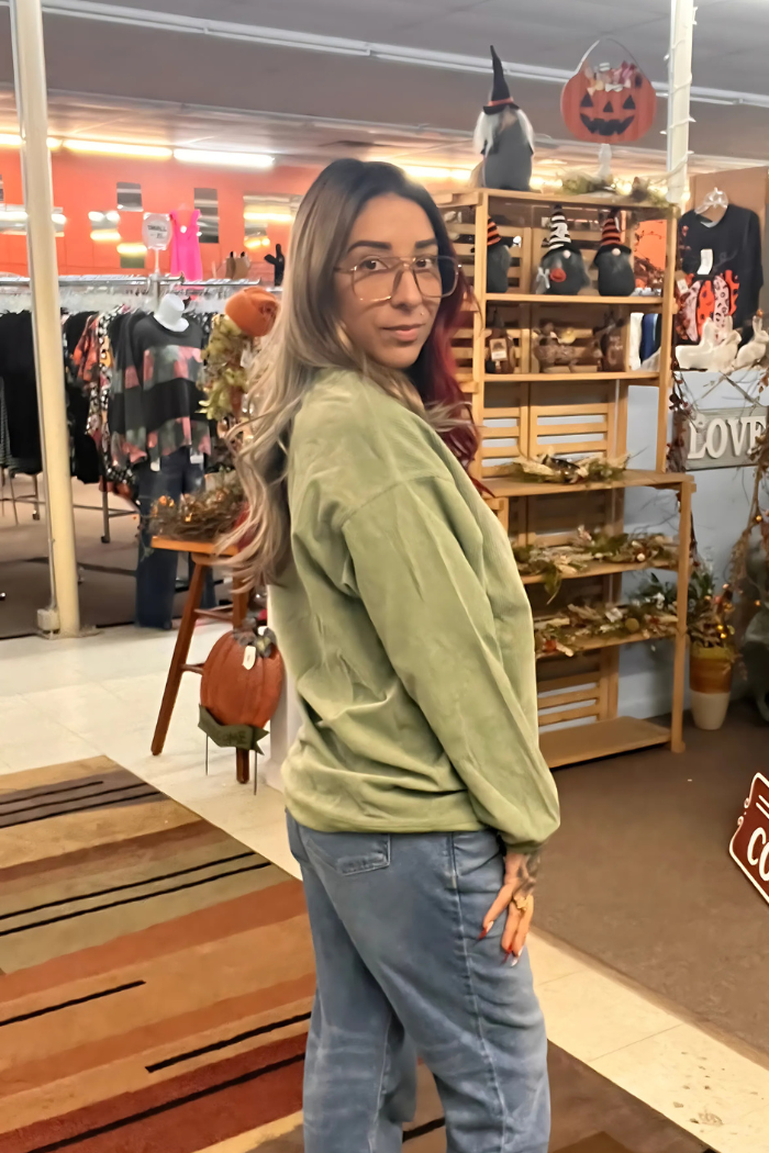 A woman wearing an olive-green oversized sweatshirt paired with blue jeans in a casual setting.