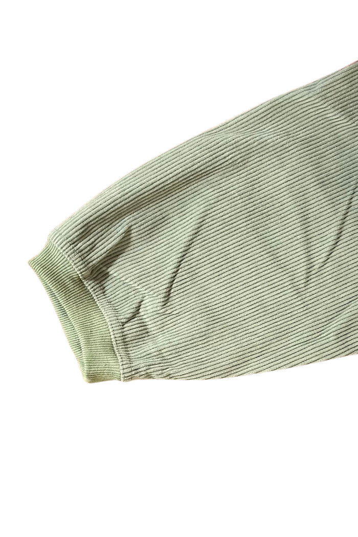 The image shows the sleeve of an olive-green, ribbed corduroy garment, sweatshirt featuring a ribbed cuff. The fabric has a distinct vertical texture characteristic of corduroy.