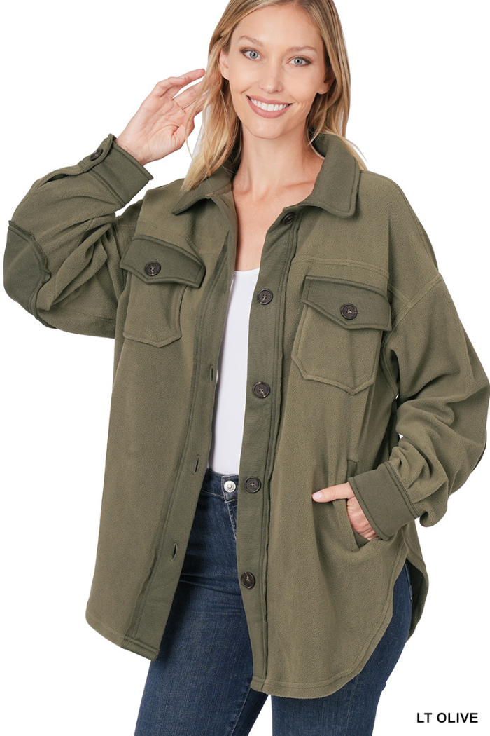 A woman with long blonde hair is smiling and looking at the camera. She is wearing a light olive green "shacket" or shirt jacket with large buttons down the front and on the cuffs, and two buttoned chest pockets. She has one hand in the pocket of the shacket. The text "LT OLIVE" is visible in the bottom right corner of the image.