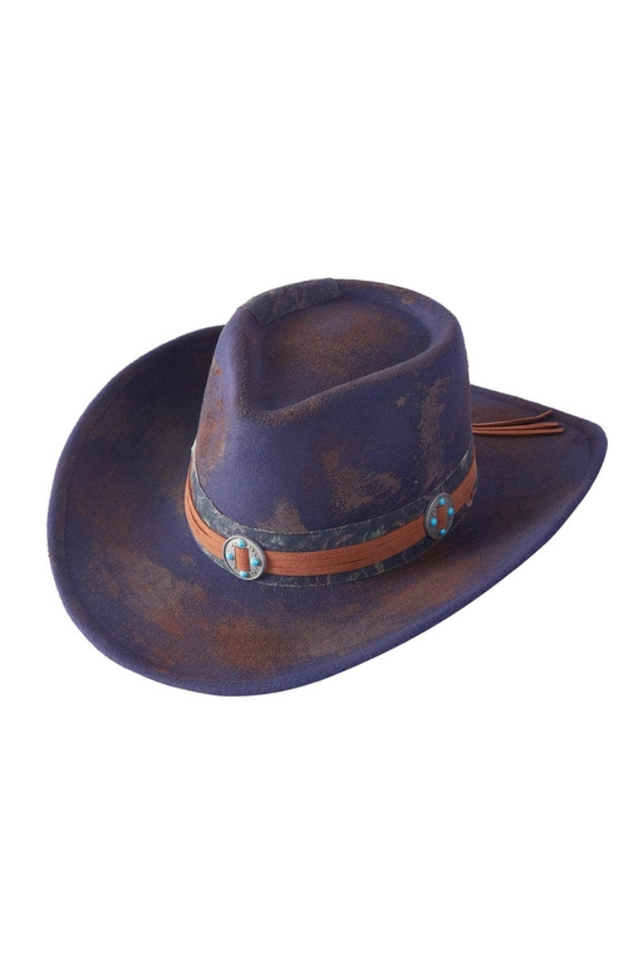 A distressed, vintage-style shapable hat, likely a blend of fedora and cowboy hat, in a dark, possibly purple or faded blue, felt-like material. It features a wide brim and a prominent brown band with turquoise-colored conchos or medallions. The hat shows visible signs of wear and aging, adding to its rustic aesthetic.