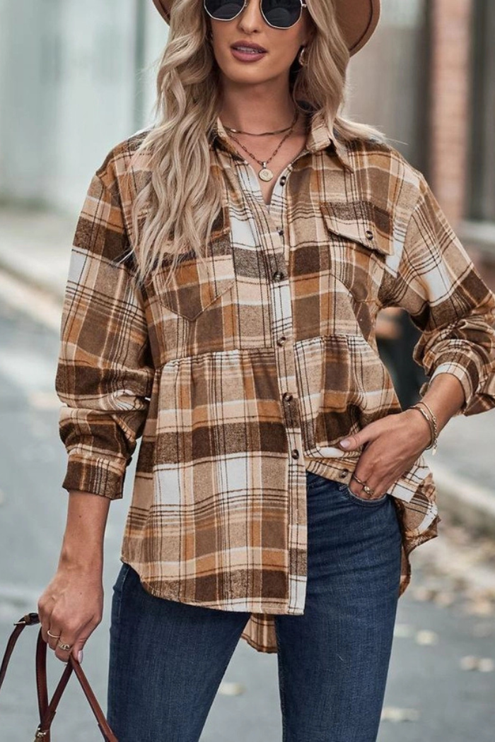 A woman is posing outdoors, wearing a stylish and casual fall outfit, including a brown and white plaid shirts layered over a white crop top, blue jeans, sunglasses, and carrying a brown handbag. She has long blonde hair and is looking towards the viewer with a slight smile. One hand in pocket.