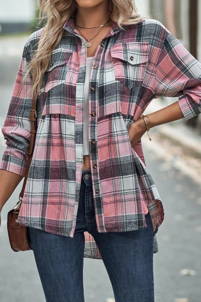 A woman viewed from the back, wearing a blue, orange, and white plaid peplum flannel shirt, paired with dark blue jeans. She stands outdoors with her hands resting on her hips.