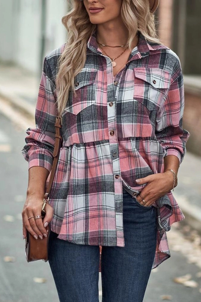 A woman wearing a pink, black, and white plaid flannel shirt over a white top, paired with blue jeans and a brown cross-body bag, with her left hand on her hip. 