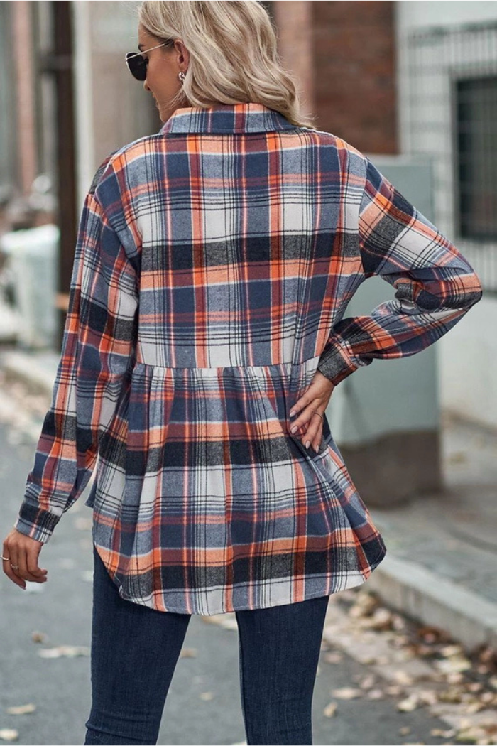 A woman from behind wears a blue, orange, and white plaid peplum-style shirt with long sleeves and a collar, paired with dark pants.