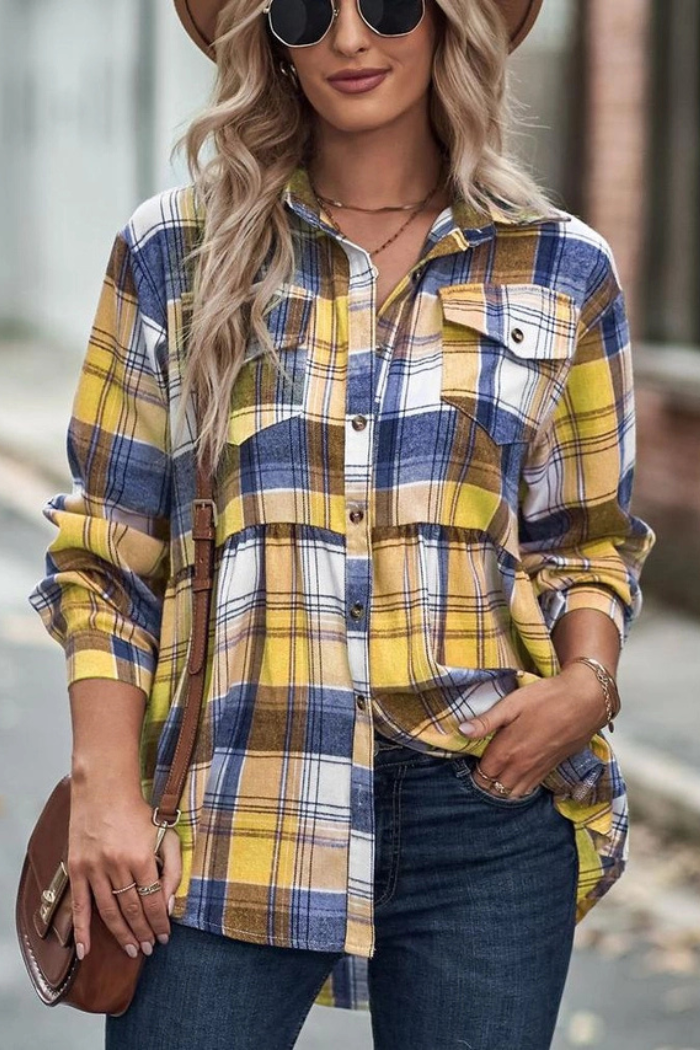 A woman is shown from the chest up, wearing a blue and yellow plaid or flannel shirt, with long blonde hair, sunglasses, and a brown shoulder bag. She is also wearing jeans and several rings on her fingers.