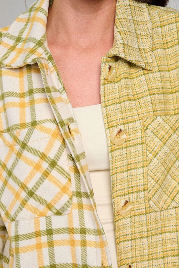 Close-up of a person wearing a plaid shacket in shades of green, yellow, and off-white, featuring a button-up front and chest pockets. 