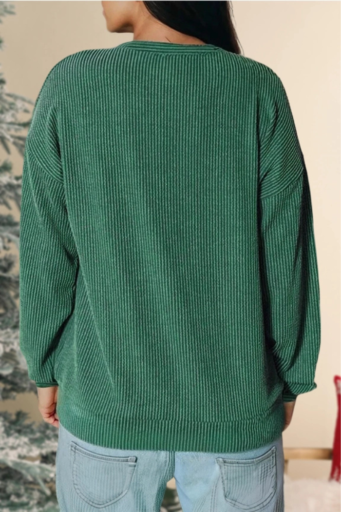 A person seen from the back, wearing a ribbed green long-sleeve top and light-wash blue jeans, with a blurred, possibly festive, background.