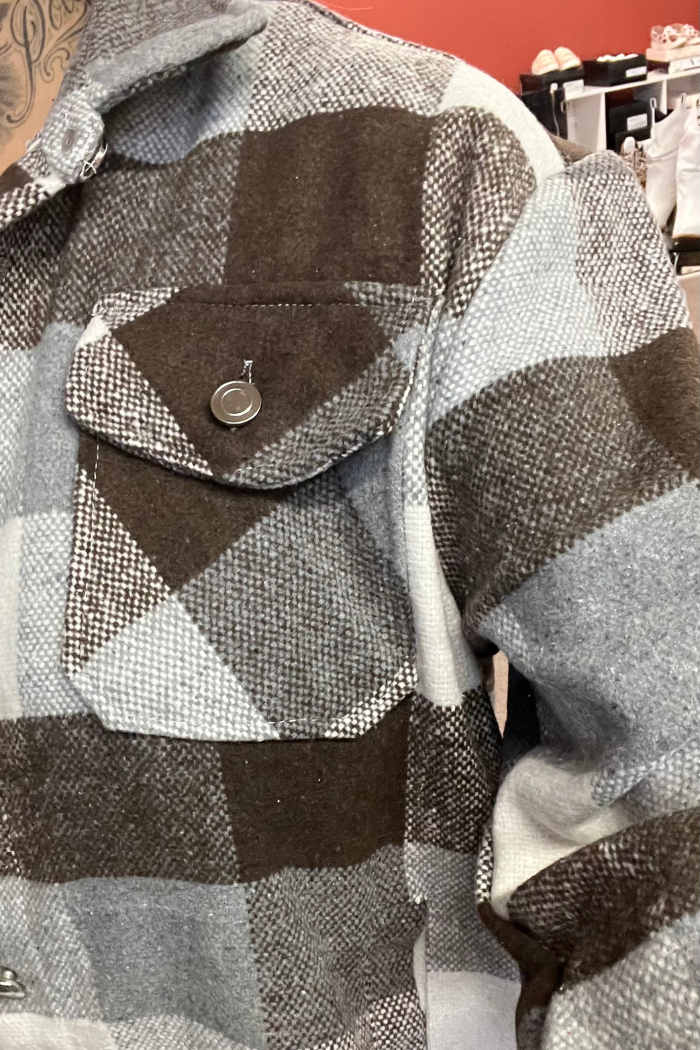 A close-up shot of a person wearing a gray, white and brown plaid shacket with a buttoned chest pocket on the left side.