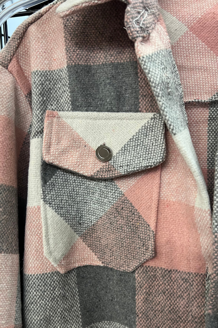 A close-up shot of a pink, gray, and white plaid flannel shacket with a buttoned chest pocket.
