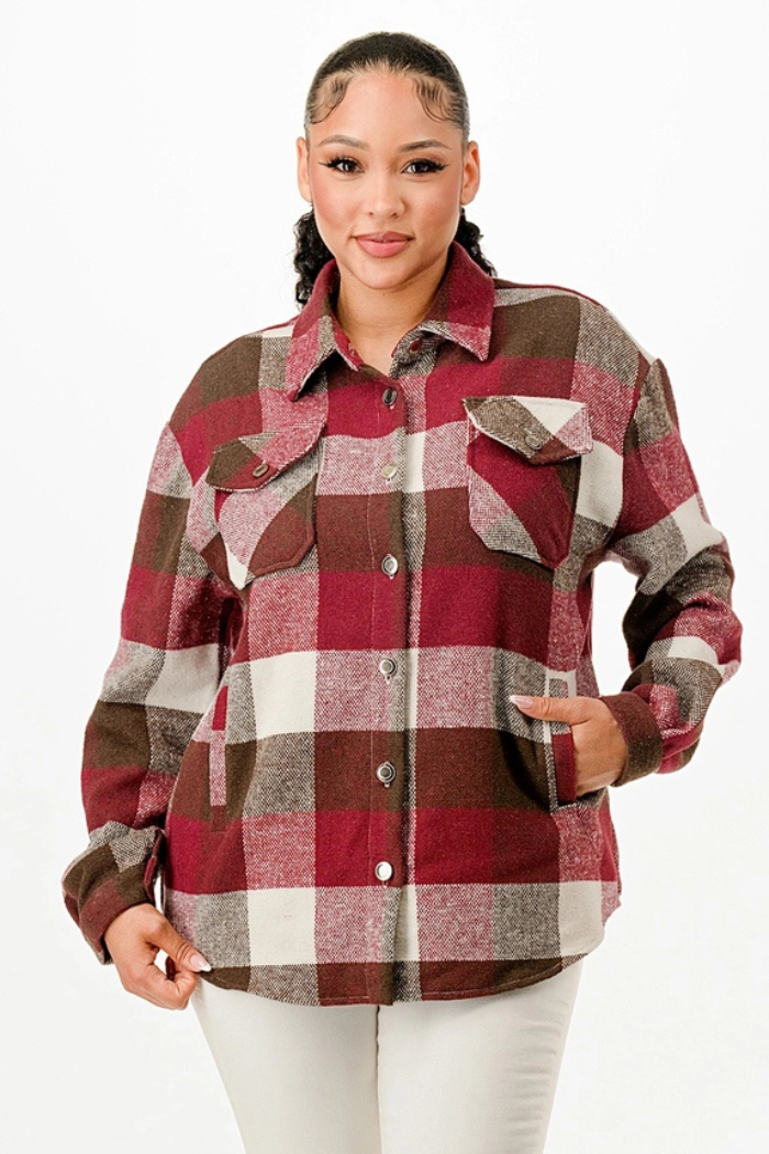 A young woman with a high ponytail, wearing a burgundy, brown, and white plaid flannel shacket over a white top and pants, with her hands in the side pockets.