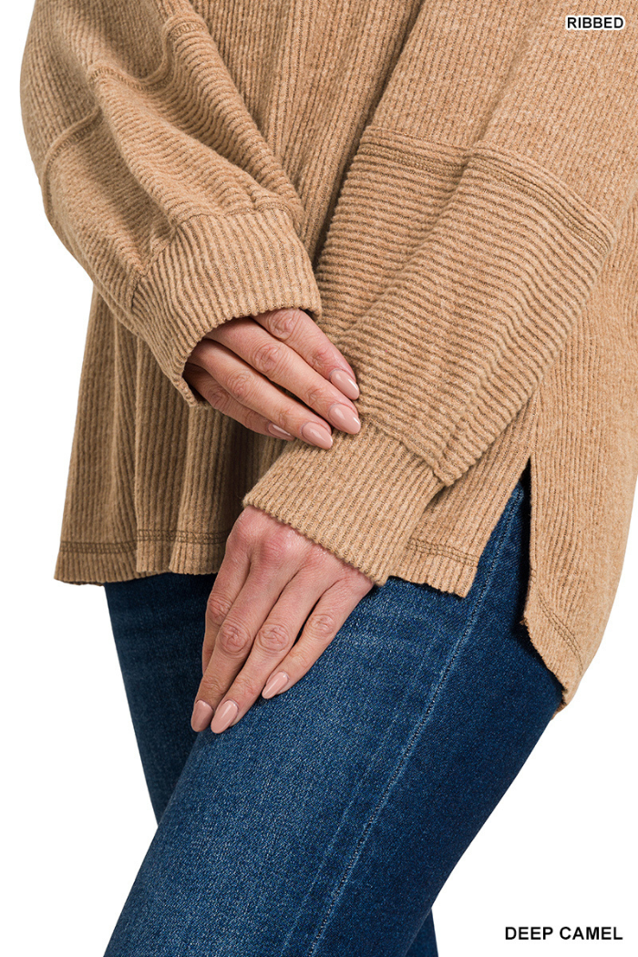 A person wears a relaxed fit, long-sleeve Brushed Ribbed Henley Top in deep camel with side slits, paired with blue jeans. Their hands are gently clasped in front. "RIBBED" and "DEEP CAMEL" are shown in the corners.