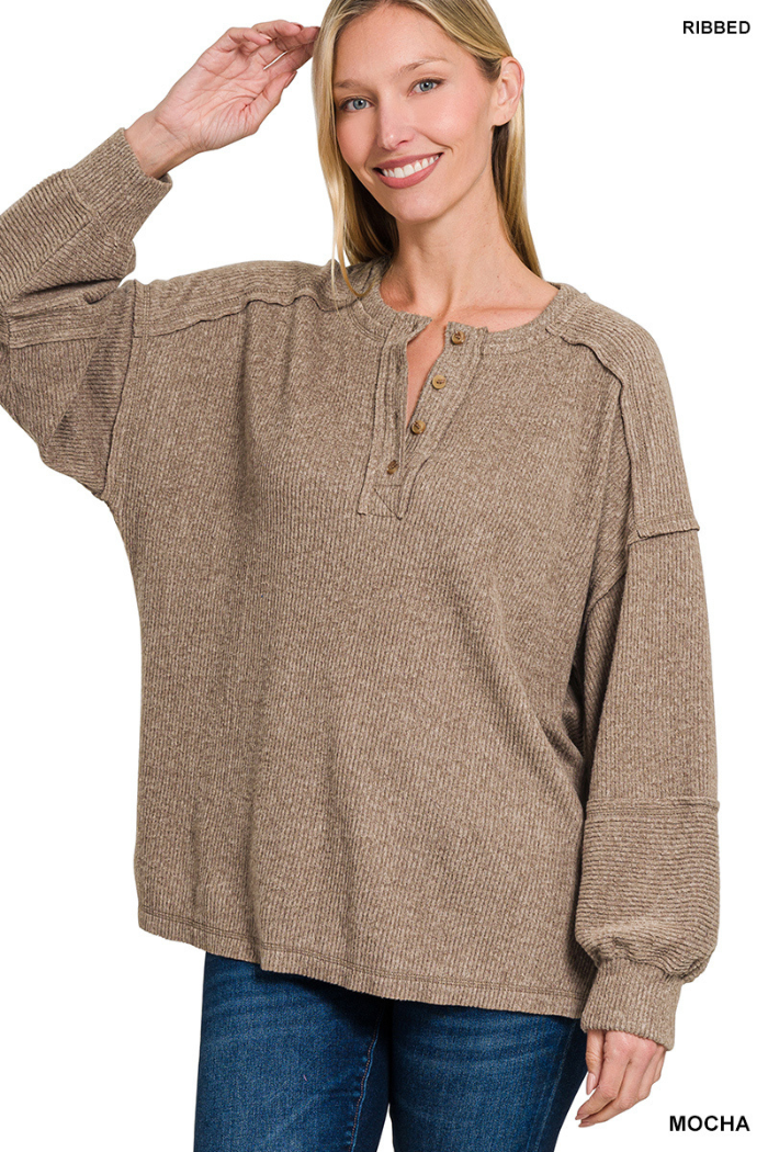 A woman smiles and raises her hand near her head, wearing a relaxed-fit Brushed Ribbed Henley Top in mocha with button details at the neckline and blue jeans—cozy loungewear for effortless style.