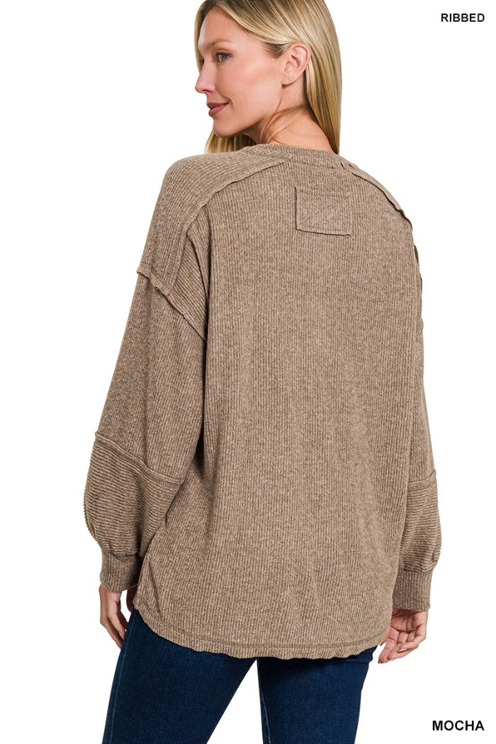 A woman with straight blonde hair wears the Brushed Ribbed Henley Top in mocha-brown with dropped shoulders and long sleeves, paired with dark blue jeans, standing against a white background, facing away.