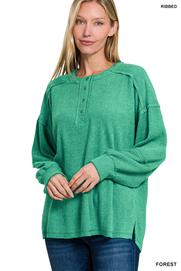 A woman with long blonde hair wears a relaxed-fit Brushed Ribbed Henley Top with button detail at the neckline and blue jeans, standing and smiling slightly against a white background, highlighting cozy loungewear style.