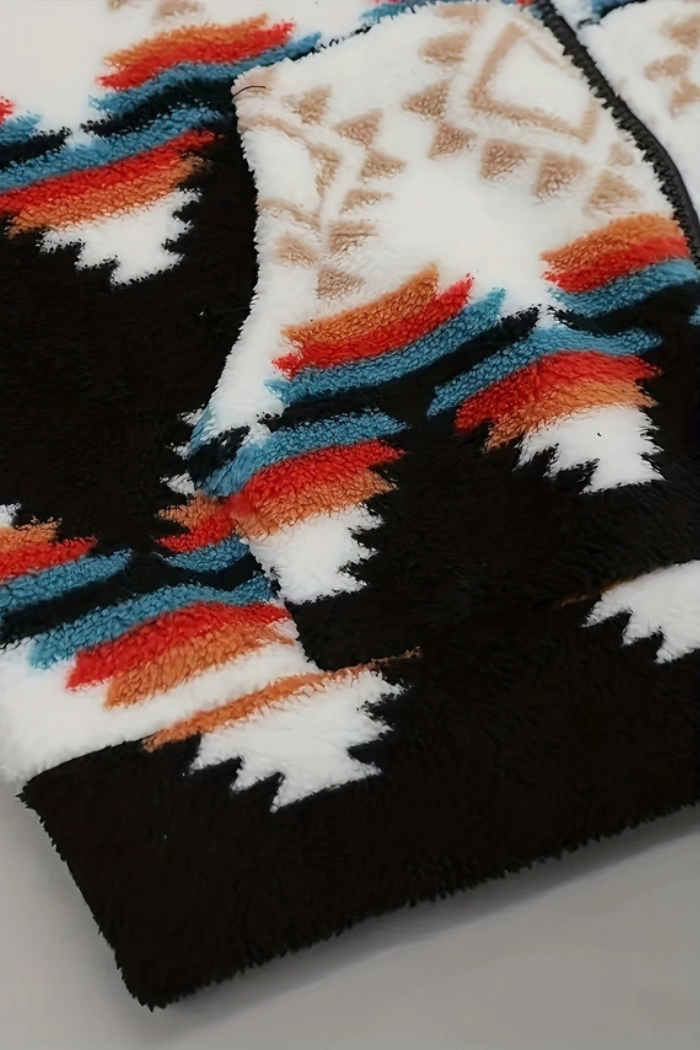 A close-up shot of a fuzzy, geometric patterned zip-up jacket. The pattern features horizontal zigzag stripes and geometric shapes in black, white, burnt orange, brown, and turquoise blue. The material appears to be sherpa or fleece. 