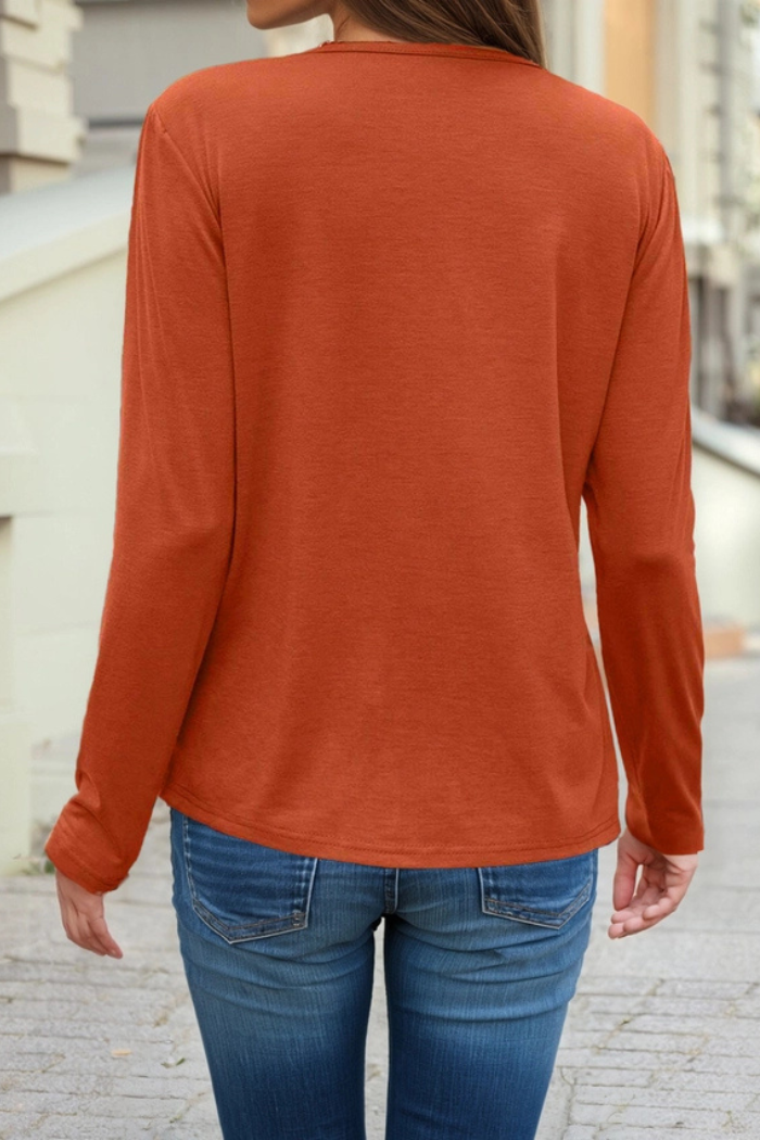 A person is shown from the back, wearing a solid, rust-orange long-sleeve shirt and blue jeans, walking on a sidewalk with buildings in the background.