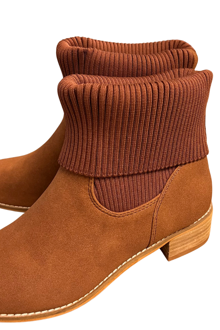 The Folded Knit Ankle Booties feature a brown suede-like finish, wooden sole, thick ribbed knit cuffs folded at the top, visible stitching along the sole, and a sock-style ankle design with one boot partly shown behind the other.