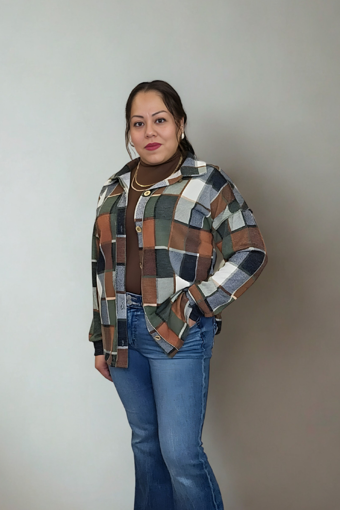 A woman stands against a plain background, confidently wearing the Plaid Print Shirt Jacket as a lightweight layer over a brown turtleneck with blue jeans and gold necklaces. Her long dark hair is pulled back as she looks at the camera.