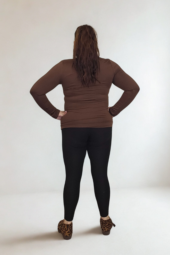 A person with long brown hair stands facing away, hands on hips. They wear the Lightweight Mock Neck Shirt, black leggings, and leopard-print wedges for a chic women's workwear look against a plain light background.
