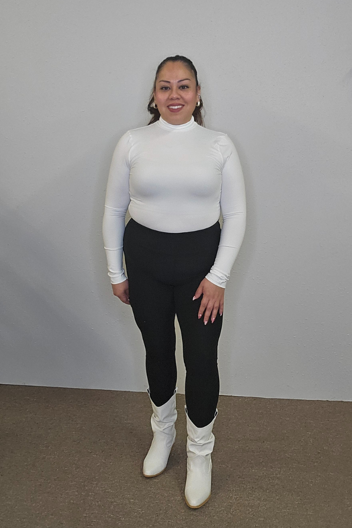 A woman smiles against a plain light wall, wearing the Lightweight Mock Neck Shirt with black pants and white boots—an ideal women's workwear look.