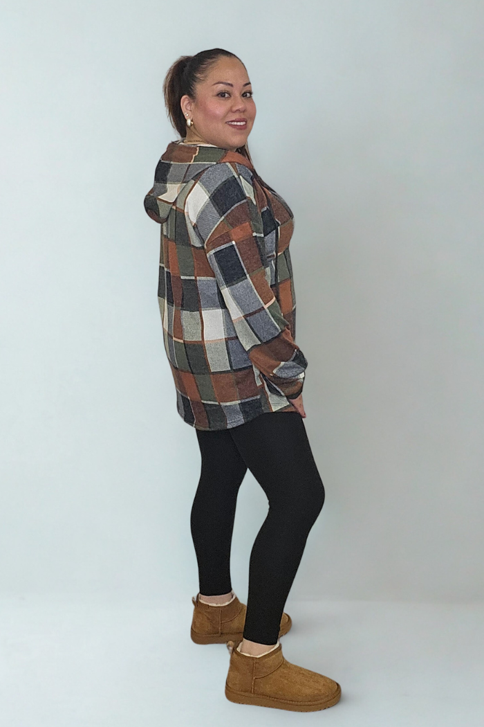 A woman stands sideways, smiling at the camera in a Plus Multi-Color Square Hoodie with a brown, gray, and white plaid design. She pairs it with black leggings and tan slippers against a plain light background.