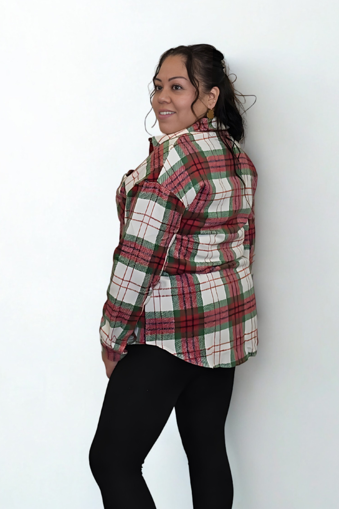 A woman with dark hair smiles over her shoulder as she stands sideways, wearing black leggings and the Christmas Plaid Flannel Shacket against a plain white background for a festive touch.