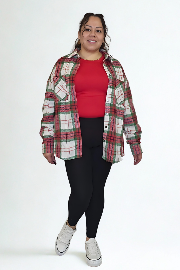 A woman smiles in a red top, black leggings, and white sneakers, topped with the Christmas Plaid Flannel Shacket styled as an oversized layer against a white background.