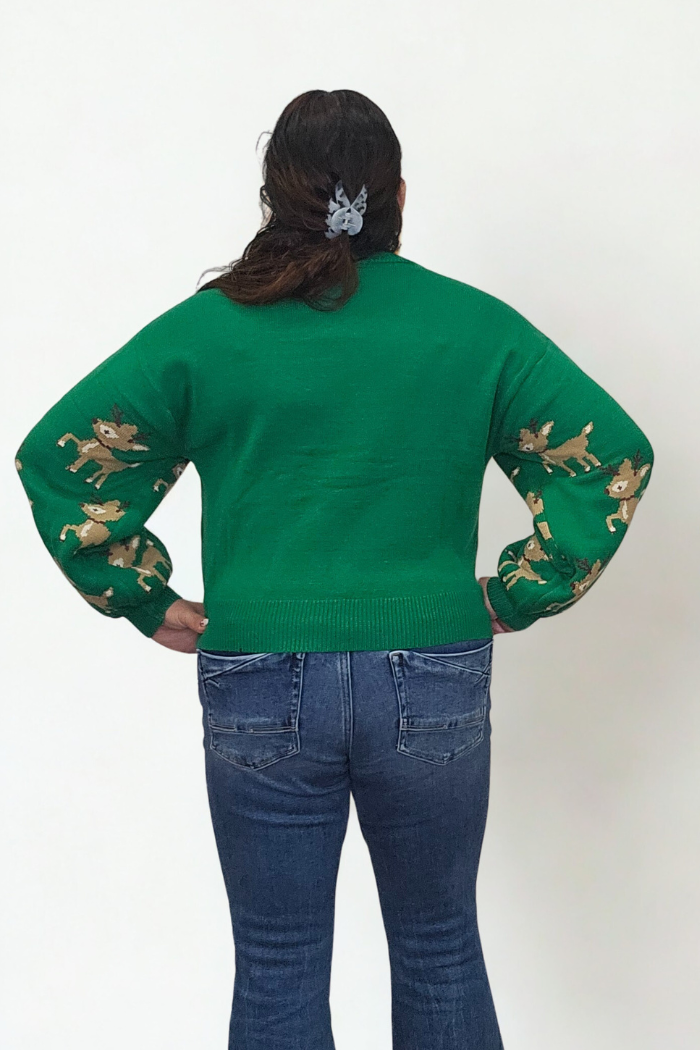 A person stands facing away, hands on hips, wearing the Slouchy Reindeer Pullover Sweater, blue jeans, and a grey hair clip against a plain white background.