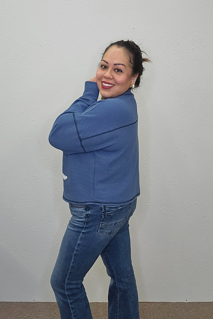 A woman wearing the Snowman Holiday Waffle Top and blue jeans stands sideways, smiling with her hand near her face against a plain light-colored wall.