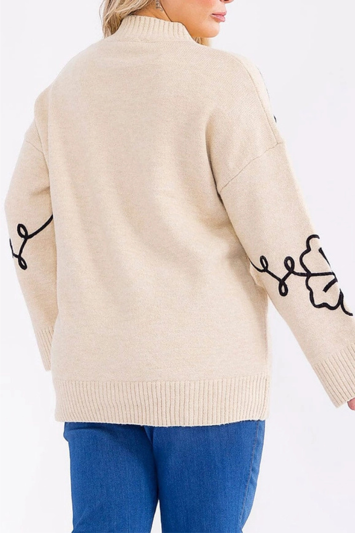 A person wearing the Floral Embroidered Knit Sweater with black floral sleeve designs and blue jeans, seen from the back against a plain light background.