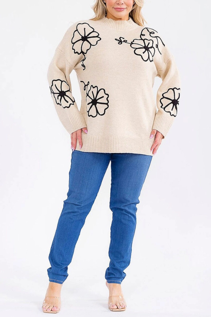 A person wearing a Floral Embroidered Knit Sweater, blue jeans, and beige open-toe heels stands against a plain white background.