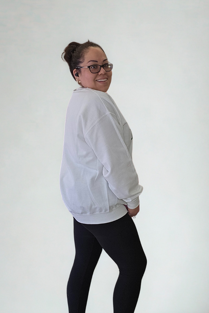 A woman wearing glasses and the Lucky Mama Sweatshirt with black leggings stands slightly turned to the side, smiling at the camera against a plain light background.