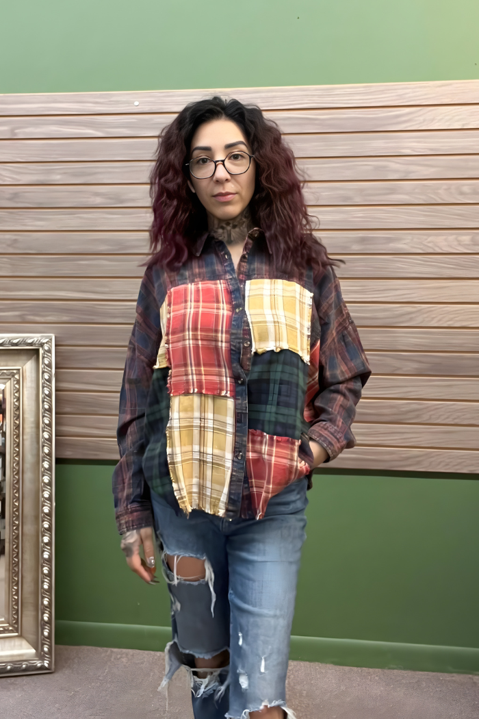 A woman with long, wavy hair and glasses models the Plaid Patchwork Button Top with ripped jeans in front of a wood-paneled wall—a perfect look for casual winter outfits.