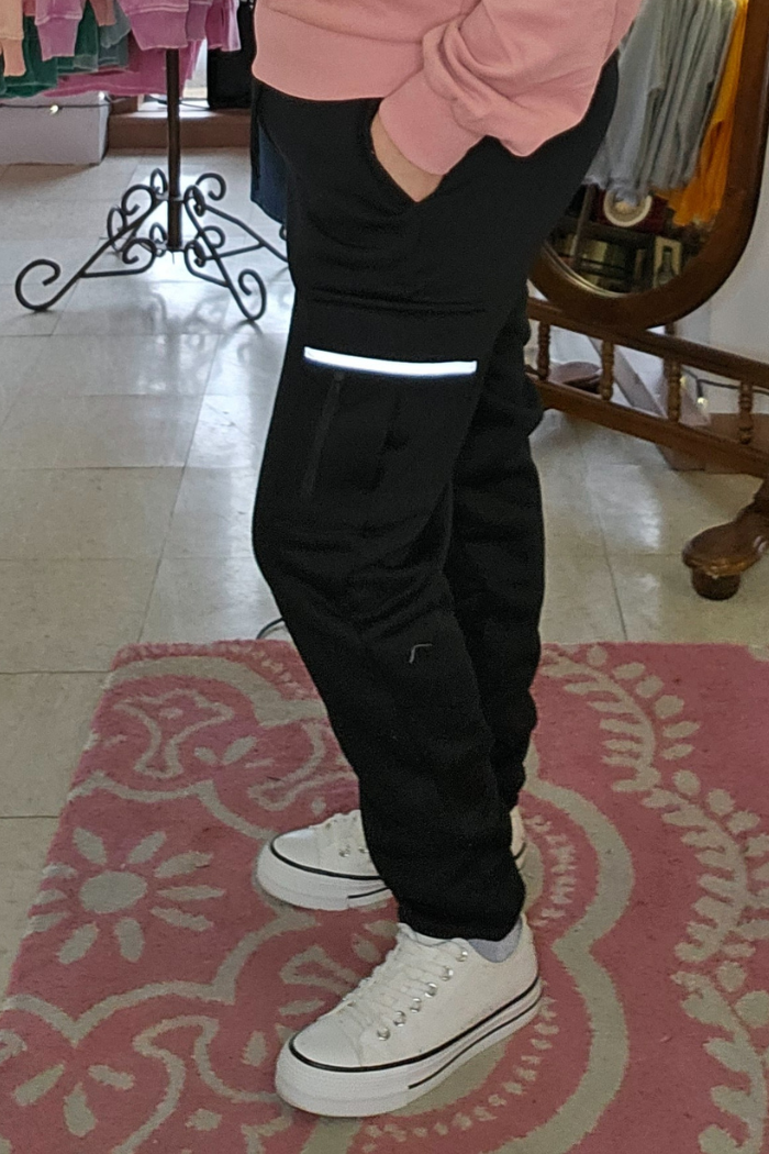 Someone wearing Fleece-Lined Cargo Joggers with a reflective stripe, white sneakers, and a pink sweatshirt stands on a pink patterned rug in a room featuring clothing racks and a mirror.