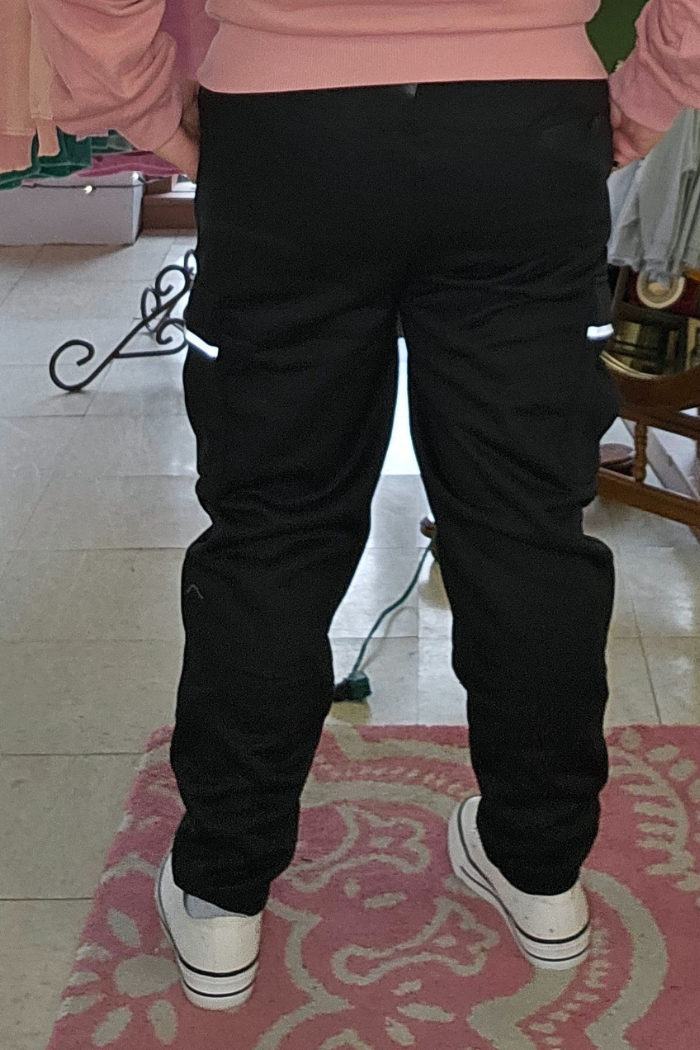 A person stands indoors on a pink floral rug, wearing Fleece-Lined Cargo Joggers with reflective strips, white sneakers, and a pink top. The photo is taken from behind.