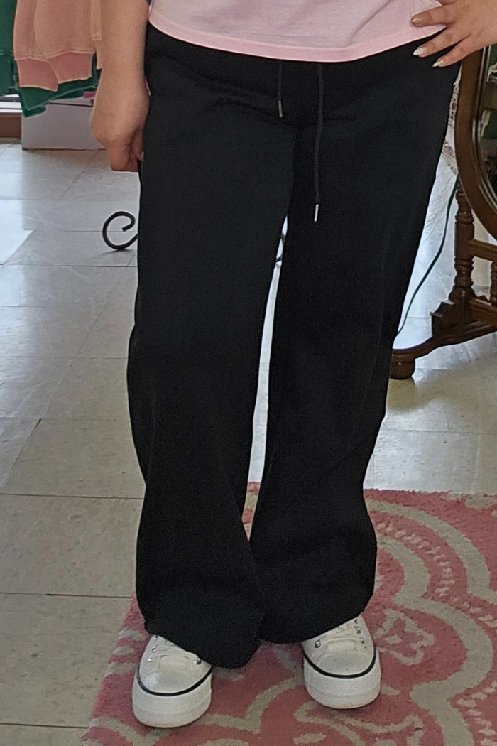 Someone wearing Wide Leg Fleece Sweatpants in black and white sneakers stands on a pink patterned rug, with only their lower half visible.