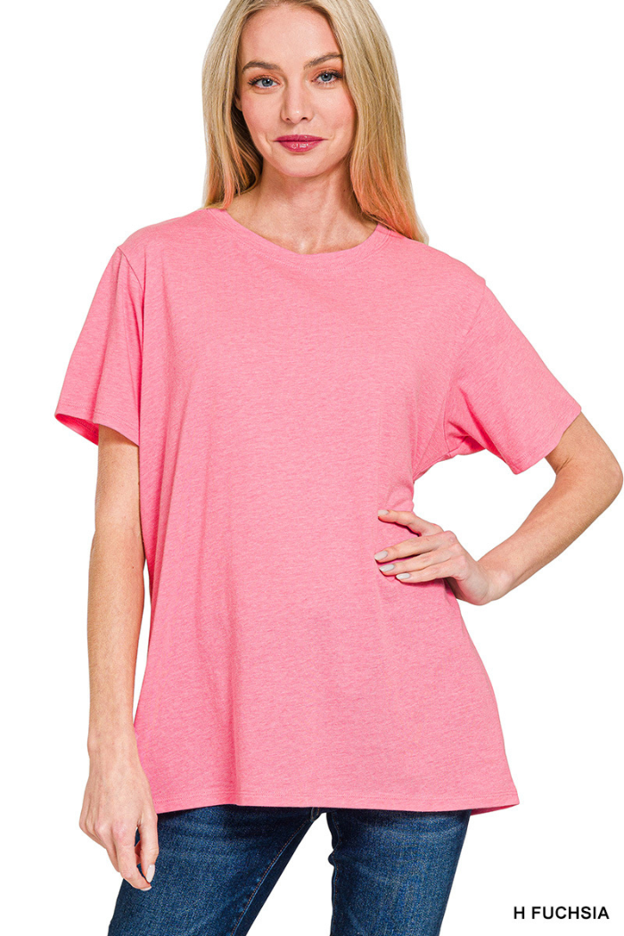 A woman wearing a relaxed fit Cotton Basic Tee in light fuchsia with short sleeves and blue jeans stands smiling at the camera, one hand on her hip, against a white background.