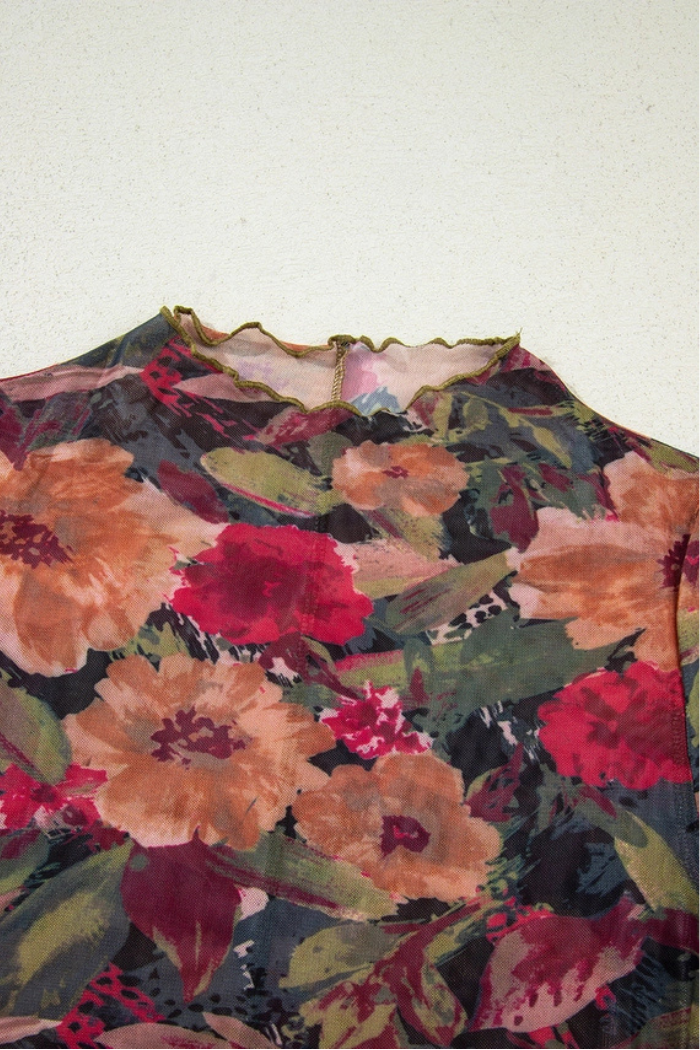 The Floral Mesh Lettuce Top features a sheer mesh fabric with red, pink, and orange flowers and green leaves on a dark base, long sleeves, a ruffled neckline, and delicate lettuce trim details.