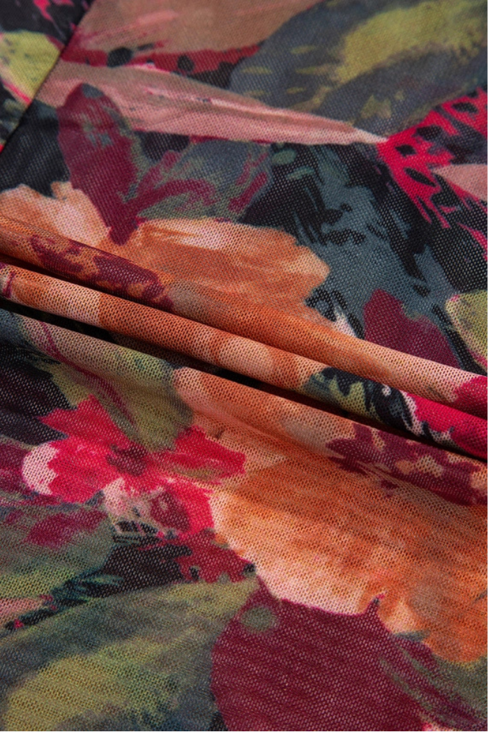 Close-up of the Floral Mesh Lettuce Top shows folded mesh fabric with vivid red, orange, green, and yellow floral designs. The texture and lettuce trim accentuate the unique overlapping patterns on this long sleeve piece.