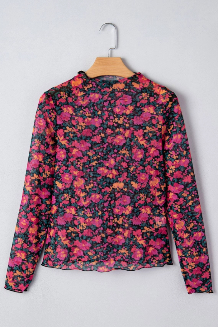 The Floral Mock Neck Top features long sleeves, lightweight mesh, and bright pink, orange, and red florals on black. Vintage-inspired and displayed on a wooden hanger against a light gray wall.
