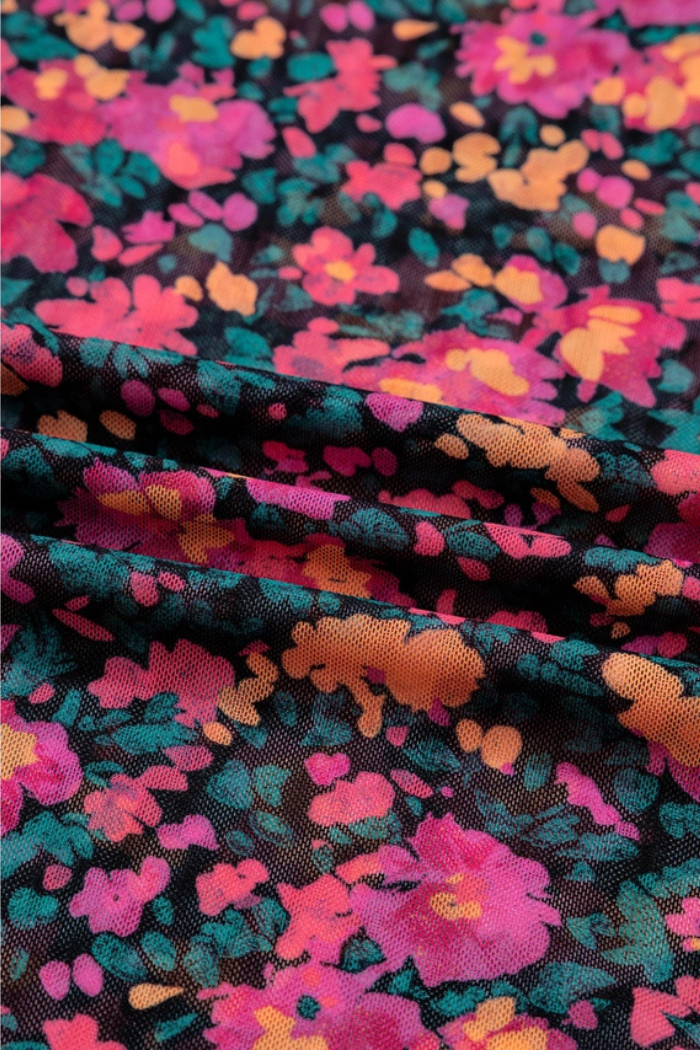 The Floral Mock Neck Top features a colorful floral print with pink, orange, and yellow flowers on a dark background. Made from lightweight mesh fabric, it has a vintage-inspired look and soft texture, perfect for comfortable layering.