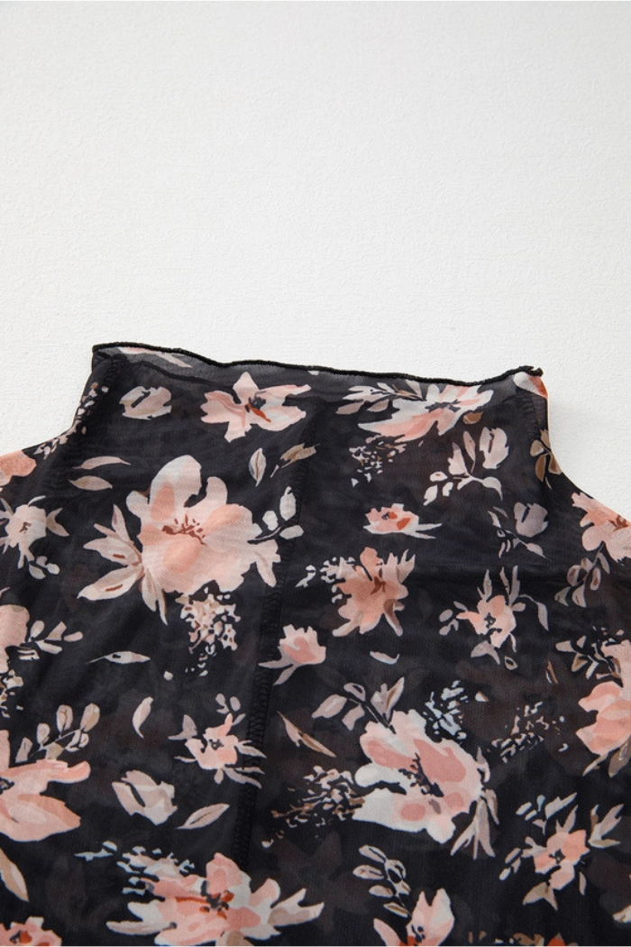 A close-up of the Floral Mesh Mock Neck Top in black, featuring pink and white floral print mesh fabric, laid flat on a white surface. The image highlights an edge detail, possibly from the neckline or shoulder area.