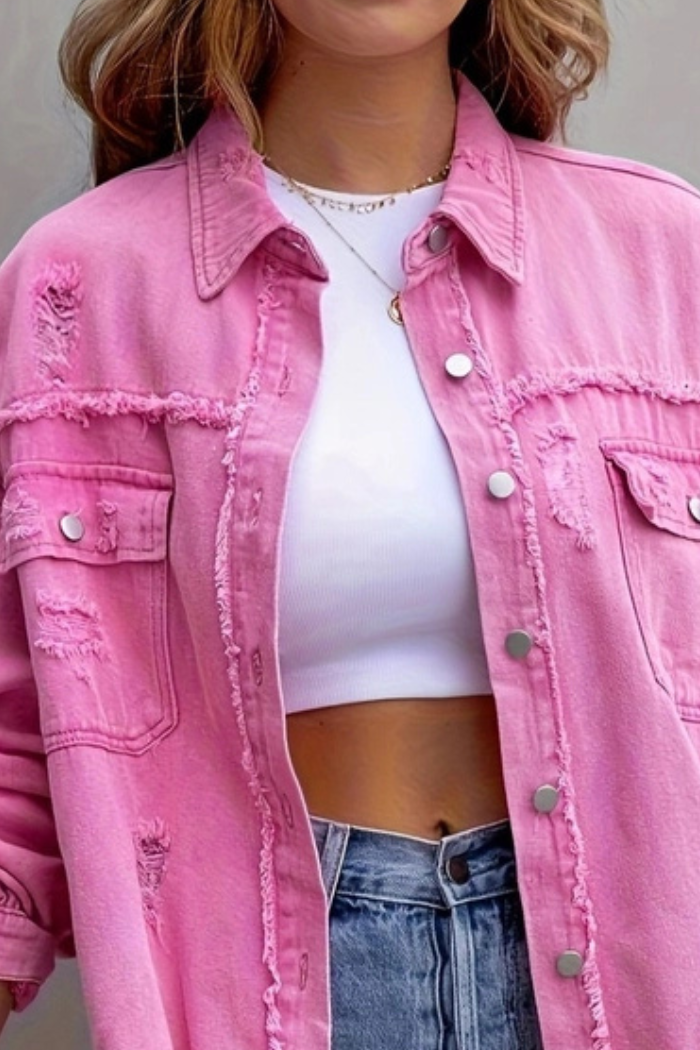 A person wearing the Ripped Edge Denim Jacket in pink, featuring frayed edges and silver buttons, styled over a white cropped top and high-waisted blue jeans. Only the torso is visible.
