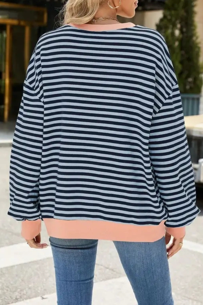 A person stands outdoors with their back to the camera, wearing the Relaxed Stripe Sweatshirt featuring navy and white stripes, peach cuffs and hem, styled with blue jeans.