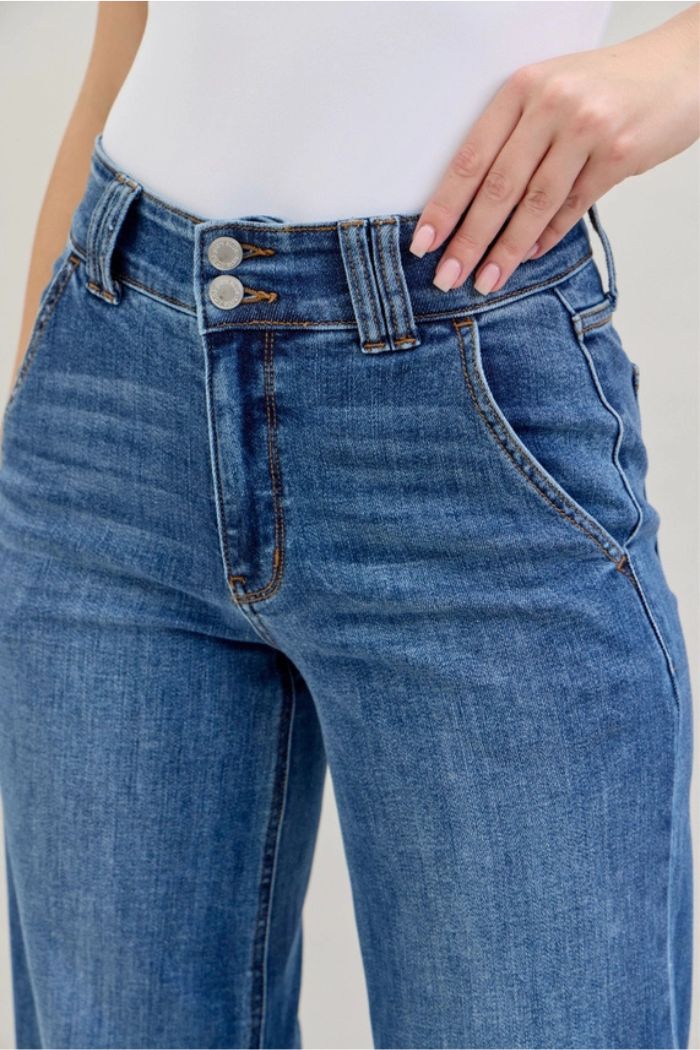Wearing High Waist Wide Leg Jeans featuring two front buttons and a wide-leg silhouette, paired with a white top; one hand rests on their hip.